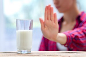 Frau mit karierter Bluse streckt ablehnend die Hand vor ein halbgefülltes Milchglas